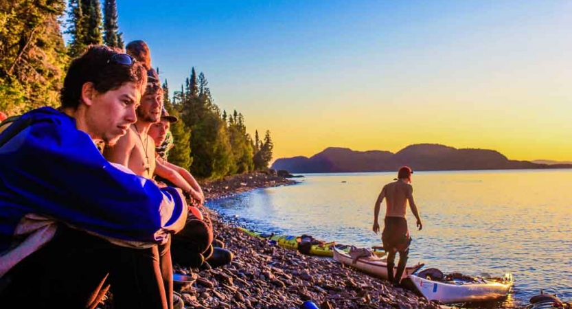 a group of outward bound students rest on the shore of blue lake after a day of kayaking